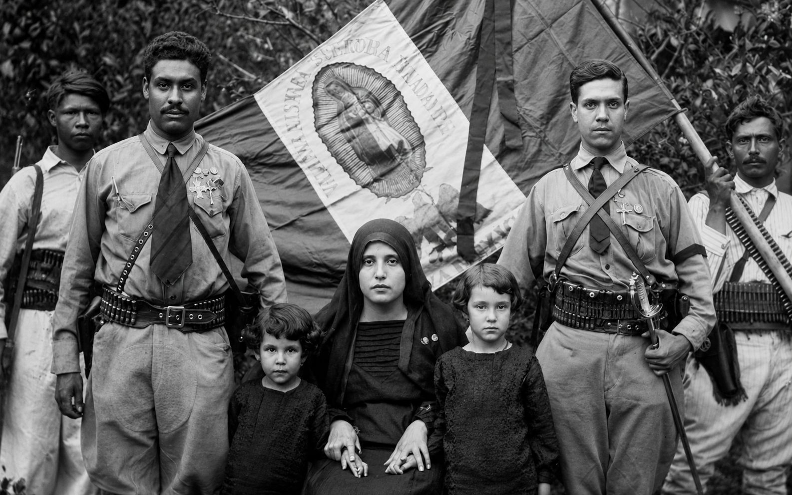 Cristeros con el estandarte guadalupano junto a una familia, circa 1927